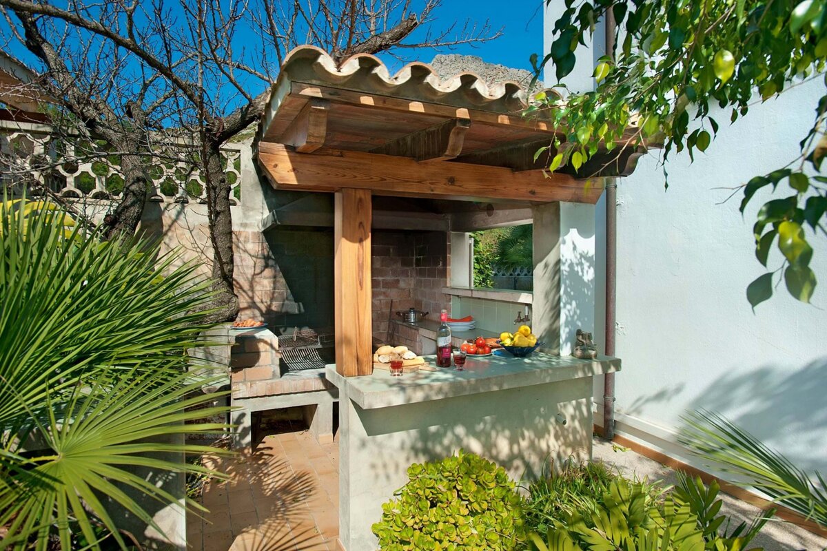 A barbecue area with a wooden roof surrounded by palm trees