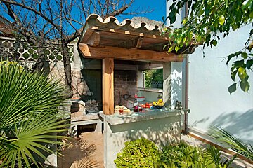 A barbecue area with a wooden roof surrounded by palm trees