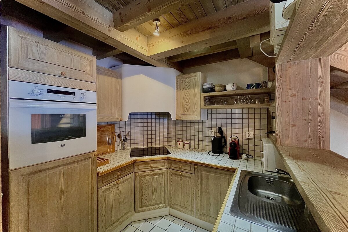 Rustic kitchen featuring light wood cabinetry, exposed ceiling beams, tiled countertops, and a built-in oven.