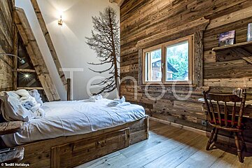 A bedroom with a bed and a desk with a picture of a tree on the wall