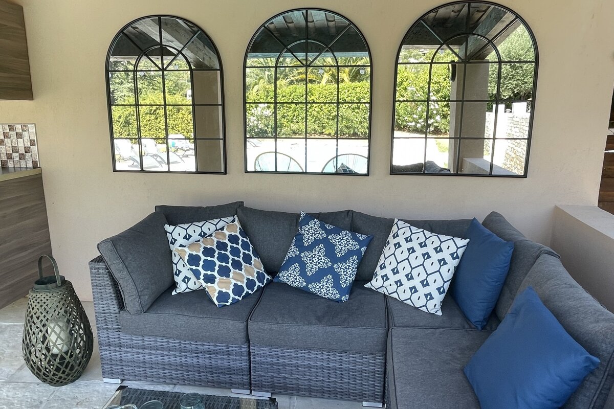 Three arched mirrors hang above a couch with blue pillows
