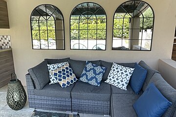 Three arched mirrors hang above a couch with blue pillows