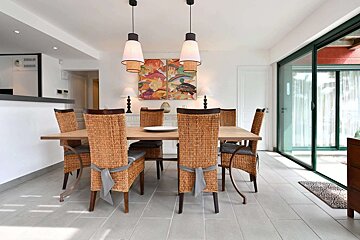 Modern dining room with a wooden table, woven chairs, and pendant lights. Features colorful fish artwork and a large sliding glass door.