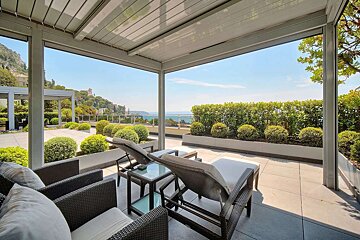 Chic terrace with modern outdoor seating, ocean views, and manicured green hedges under a clear sky.