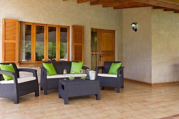 A patio with a couch and chairs with green pillows