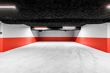 Modern, empty parking garage with a white-and-red wall, black textured ceiling, linear lights, and tire tracks on the concrete floor.