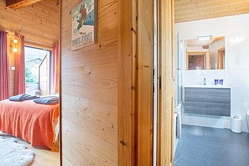 Wooden cabin interior showing a bedroom with an orange bedspread on the left and a modern bathroom on the right.