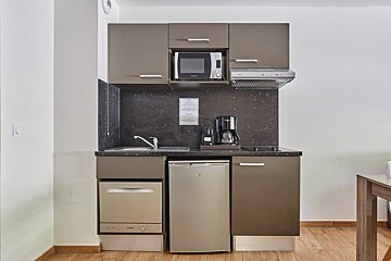 A compact kitchenette features brown cabinets, a black marble-look counter/backsplash, microwave, coffee maker, fridge, dishwasher, and stovetop.