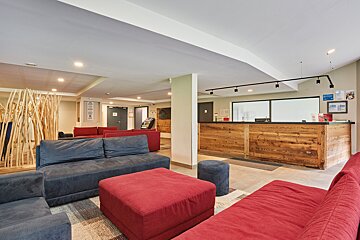 A welcoming lobby with a rustic wooden reception desk, comfortable red and blue sofas, and a stylish wooden room divider.