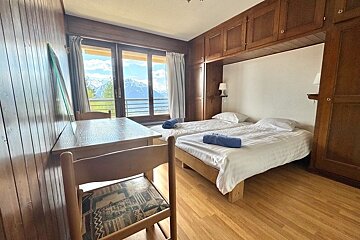 Cozy wood-paneled bedroom featuring twin beds, a dining table, and a balcony offering a scenic mountain view.