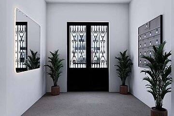 A modern entryway features ornate black double doors, a backlit mirror, multiple potted palm plants, and a wall-mounted mailbox system against white walls.