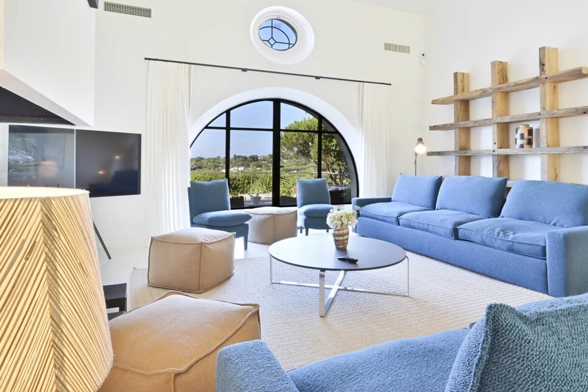 Modern living room with white walls, blue seating, a large arched window, and an outdoor scenic view.