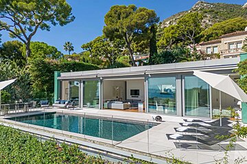 Luxurious modern villa with a sparkling pool, glass doors, and outdoor living space, nestled in lush greenery with mountains in the background.
