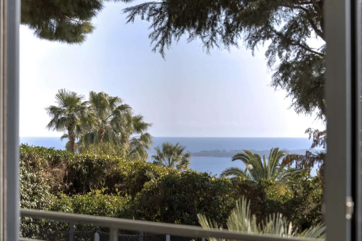 A view of the ocean through a window with palm trees in the foreground