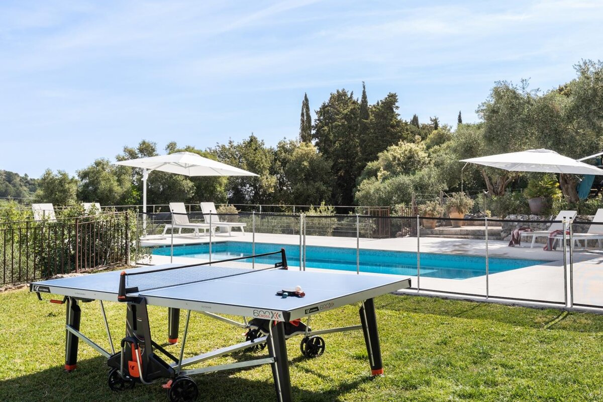A ping pong table sits in the grass near a pool