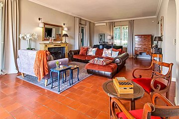 A classic living room with warm terracotta floors, a fireplace, and comfortable sofas in rich red and light purple, set with game tables.