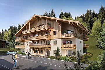 A large, new chalet-style building with many wooden balconies, nestled in a forested mountain landscape. People are in the foreground parking area.
