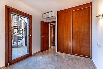 An empty room with marble floor, wooden door to a spiral staircase, built-in closet, AC unit, and an open doorway to a hallway.