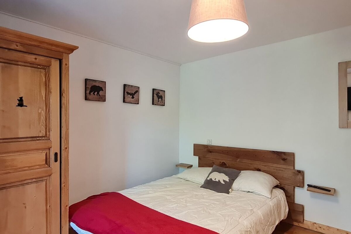 A cozy, rustic bedroom featuring a wooden bed with a red throw, a matching wooden wardrobe, and animal-themed wall art.