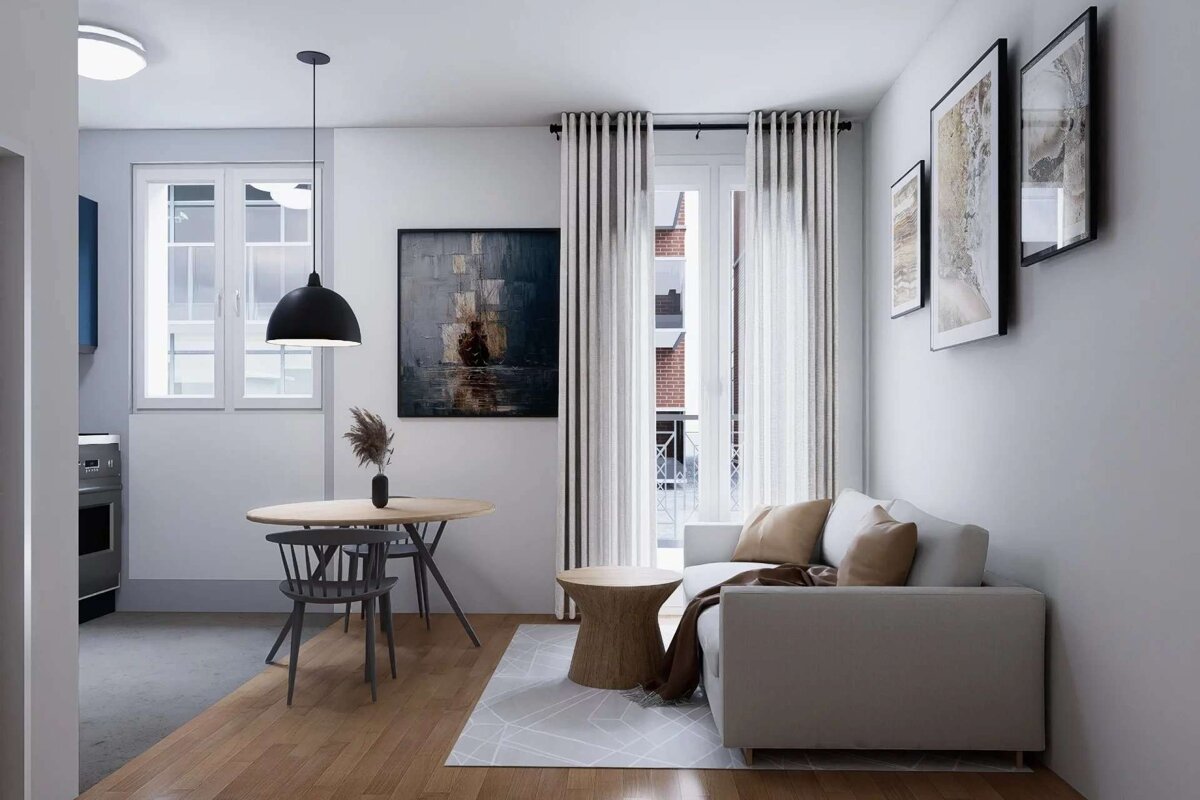 A modern open-plan living/dining space with a light sofa, wooden furniture, and framed art, illuminated by natural light and a pendant lamp.