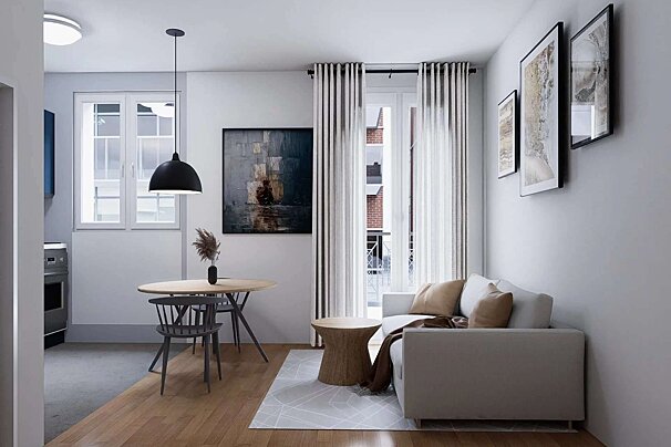A bright, modern open-plan living area with white walls, wooden floors, a round dining table, sofa, artwork, and a large window.