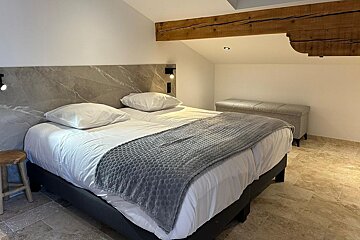 A bed with white sheets and a grey blanket
