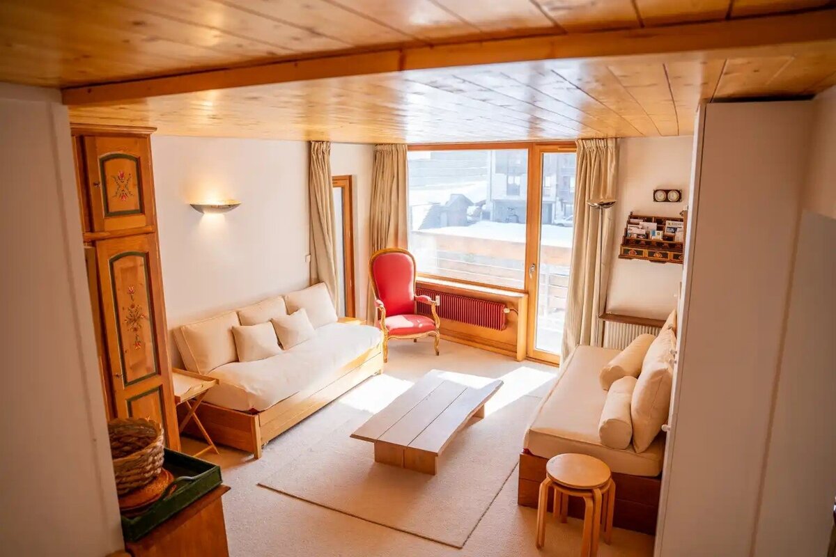 A cozy, wood-paneled living room with two beige sofas, a low coffee table, a red armchair, and large windows.