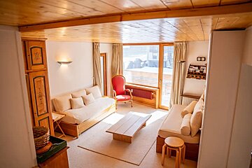 Cozy chalet living room with wooden ceilings, two beige sofas, a red armchair, and a low wooden coffee table.