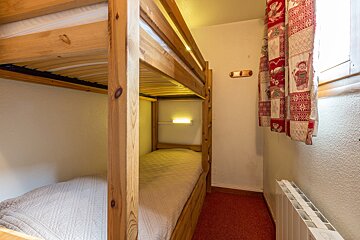 A cozy room features wooden bunk beds, red patterned curtains next to a window, a red carpet, and a heater. A reading light is present on the bottom bunk.