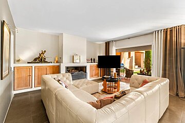 A bright living room features a large white sectional sofa, a fireplace, a TV, and opens to a sunlit outdoor patio.