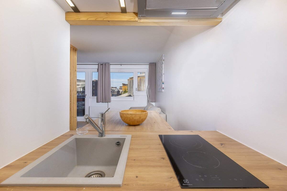 Modern kitchen counter with a sink and induction hob in the foreground, looking into a bright room with a large window and city views.