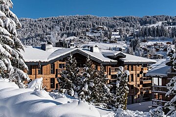 A charming mountain village covered in fresh snow, featuring wooden chalets and frosted fir trees against a clear blue sky.