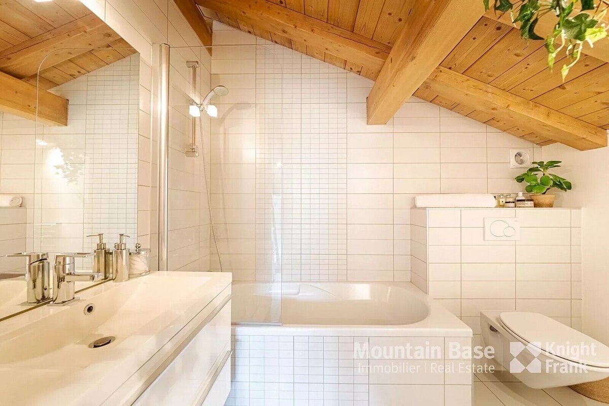 A bathroom with white tiles and a wooden ceiling from mountain base