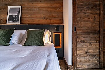 A cozy bedroom with a white-sheeted bed, plush green pillows, a rustic wooden headboard, and a matching wooden sliding door, creating a warm ambiance.