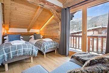 A bedroom with two beds and a balcony with mountains in the background