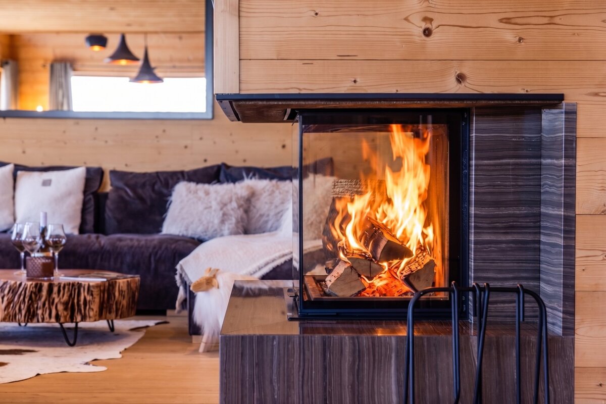 A modern glass fireplace burns brightly in a cozy, wood-paneled chalet living room with a comfortable sofa in the background.