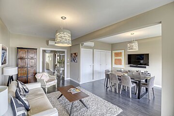 A spacious living and dining area with neutral decor, featuring a cream sofa, dark wood dining set, a large rug, and modern pendant lights.