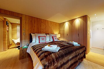 A bedroom with a fur blanket and pillows with hearts on them
