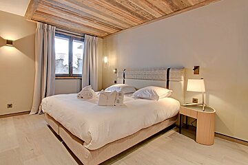 Cozy bedroom with a large bed, light wood floor & ceiling, white bedding, and modern lighting. A window shows a snowy view outside.