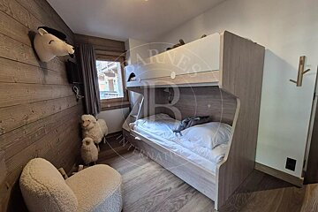 A cozy, wood-paneled bedroom features modern bunk beds, a window view, and playful decor including a bear head, plush sheep figures, and a fluffy chair.