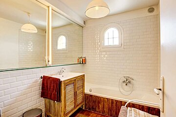 A bright bathroom features white subway tiles, a wooden vanity, and a bathtub. An arched window and large mirror complete the clean, rustic-modern look.