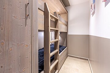 A cozy room features light wood bunk beds with dark blue bedding, an integrated wardrobe, and walls painted two-tone white and taupe.