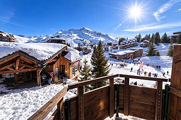 Sunny winter day at a vibrant mountain ski resort. Snow-covered wooden chalets and slopes filled with people, against a backdrop of majestic peaks.
