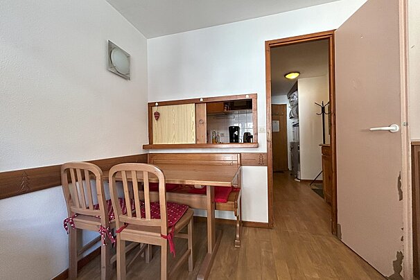 A cozy dining area features a wooden table, chairs, and a built-in bench, with a pass-through to a compact kitchen. An open doorway leads to a hall.