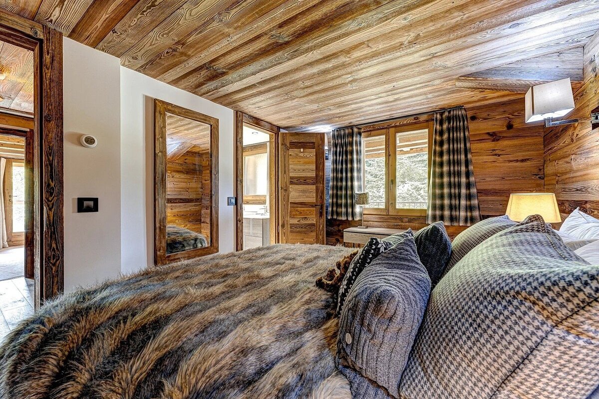 Cozy, rustic bedroom with rich wooden walls and ceiling, a plush faux fur blanket, and a window view to the outdoors.