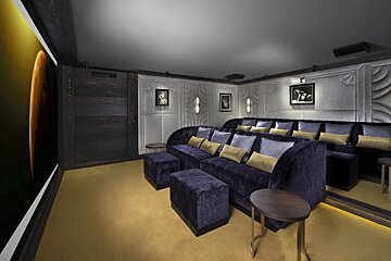 A luxurious home cinema with tiered dark purple velvet seating, a gold carpet, and a large screen displaying a celestial scene. Elegant modern design.