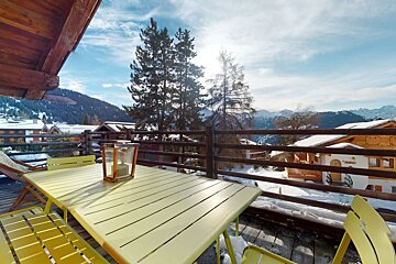 A table with a lantern on it sits on a balcony overlooking snowy mountains