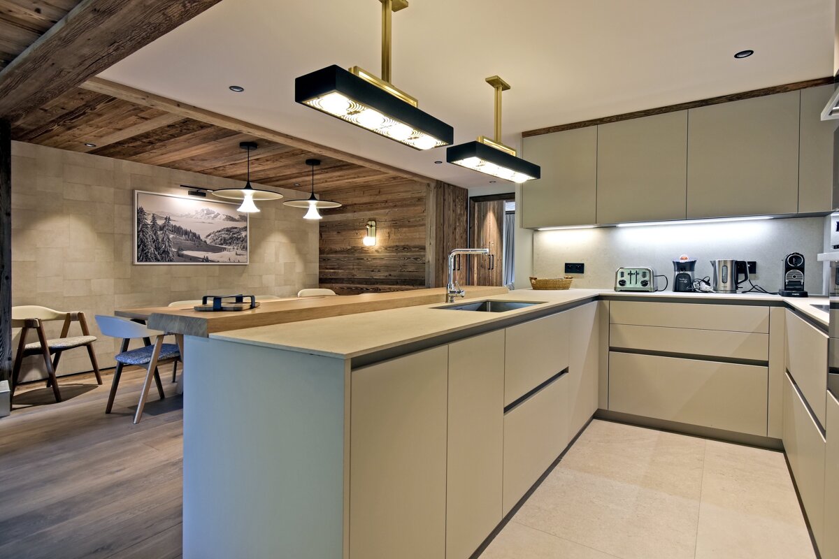 Modern chalet kitchen featuring cream cabinets, a large island, stylish pendant lights, and a rustic wood dining area.