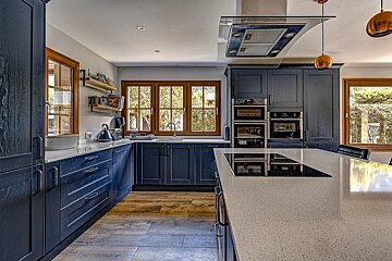 Modern kitchen with dark blue cabinets, light countertops, and a central island featuring an induction hob, all bathed in natural light.