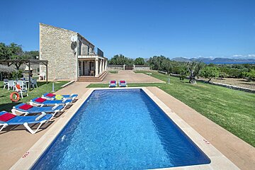 A large swimming pool is surrounded by lawn chairs and a house